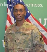 c/MAJ Andrew Hargrett posing in front of green background and U.S. flag. 